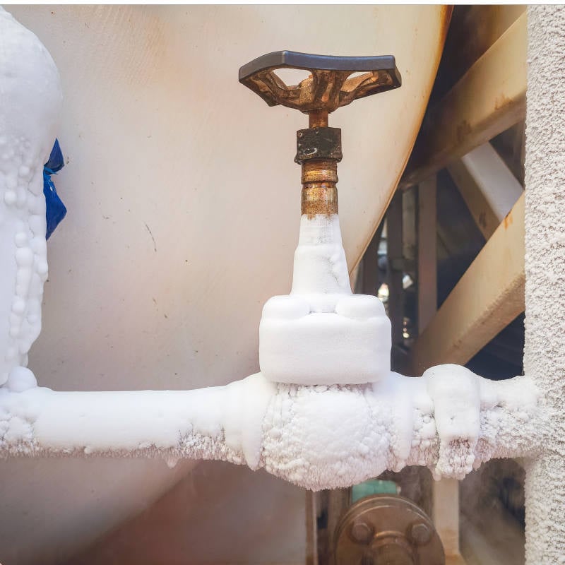 A metal valve and pipe covered in frost and ice, indicating exposure to extremely cold temperatures or handling of cryogenic substances, often seen before line thawing operations.