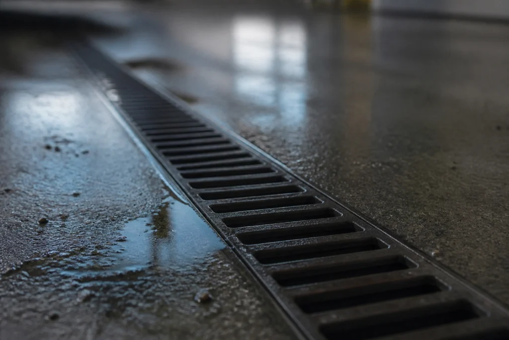 Close-up of a wet concrete floor with a metal drainage grate, often found in car wash sand trap areas where slow drains or strange smells can be an issue.